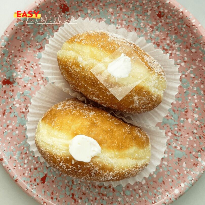 Beignets à la crème pâtissière vanille et chocolat saupoudrés de sucre et cacao sur une assiette.