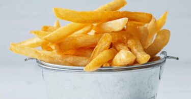 Frites surgelées dorées et croustillantes sorties de l’airfryer, servies dans un panier métallique.