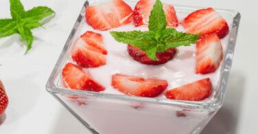 Yaourt maison à la fraise servi dans un pot en verre avec des morceaux de fraises fraîches