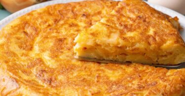 Tortilla de pommes de terre dorée et moelleuse, coupée en parts, servie avec une salade.