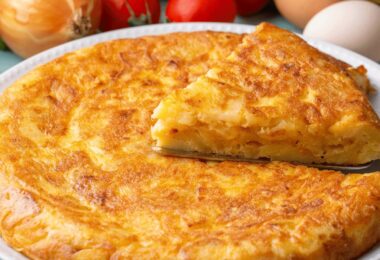 Tortilla de pommes de terre dorée et moelleuse, coupée en parts, servie avec une salade.