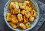 Tofu croustillant doré et assaisonné, servi avec une sauce et des herbes fraîches.