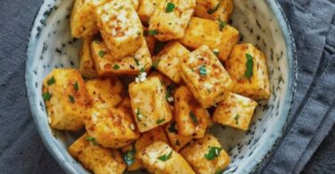 Tofu croustillant doré et assaisonné, servi avec une sauce et des herbes fraîches.