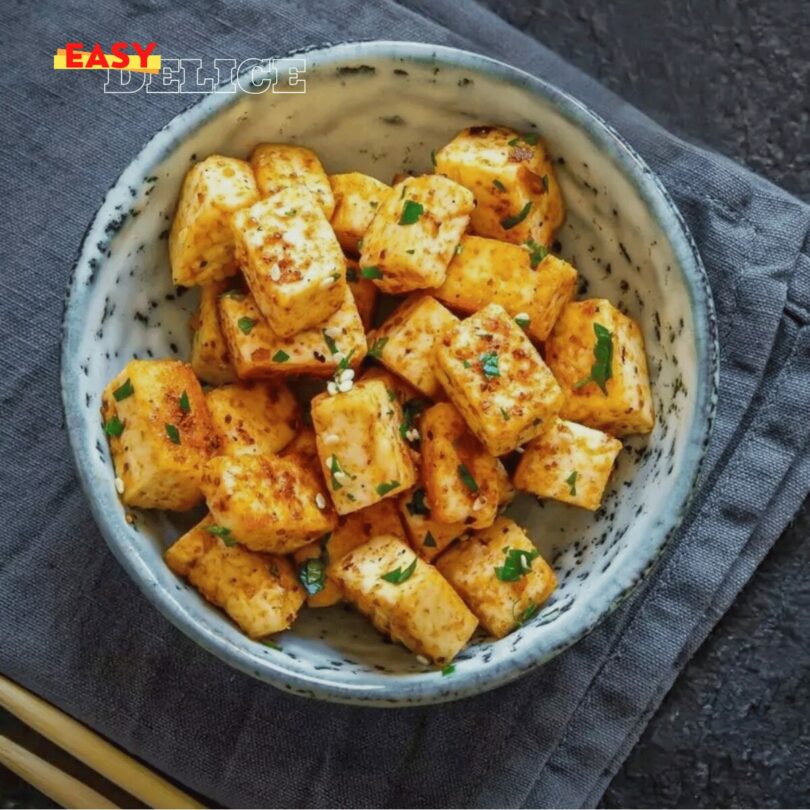 Tofu croustillant doré et assaisonné, servi avec une sauce et des herbes fraîches.