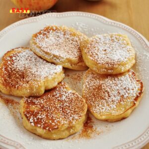 Pancakes aux pommes dorés empilés, garnis de tranches de pomme et d’un filet de miel.